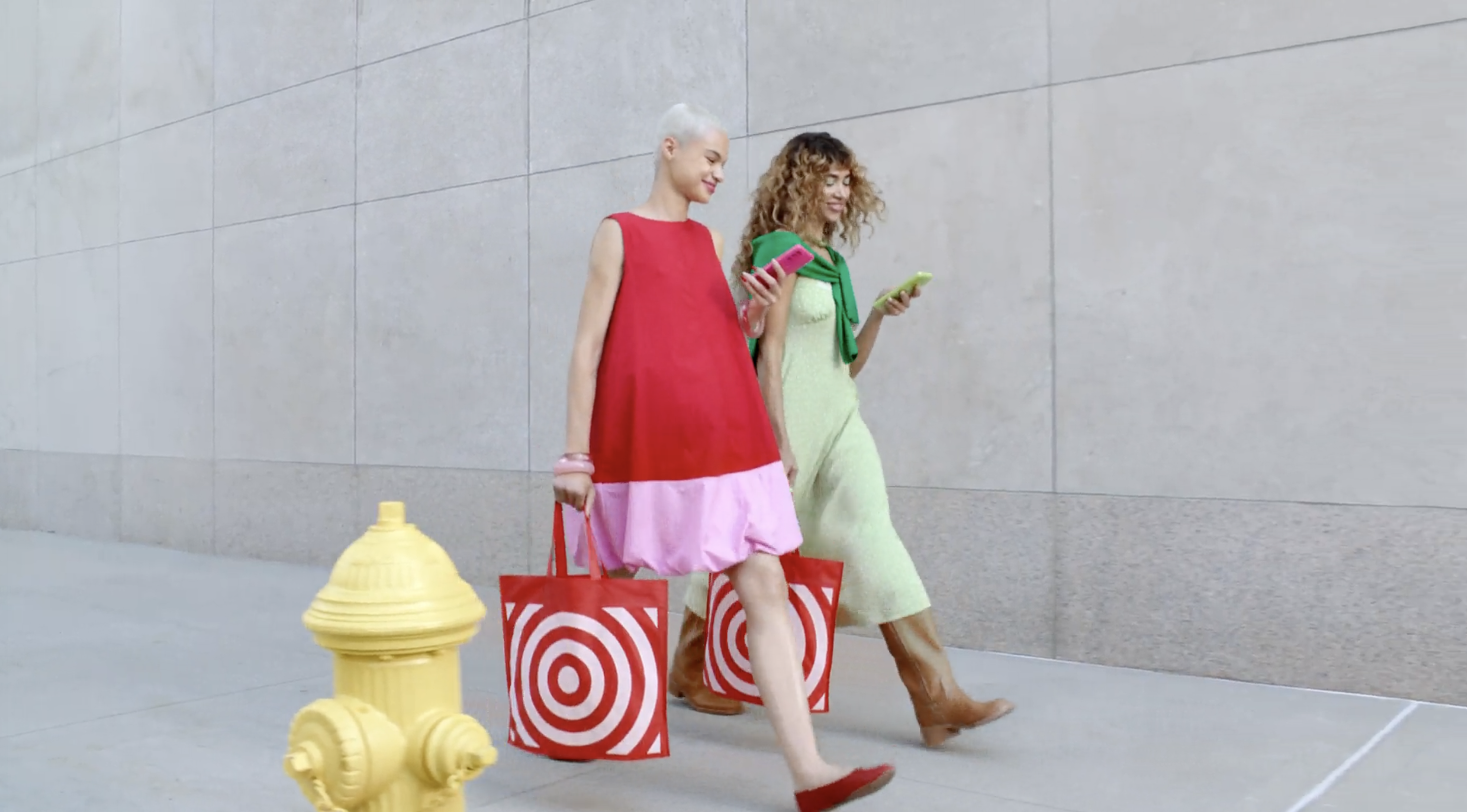 Two women in red and pink and green dresses walking past a yellow fire hydrant